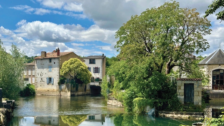 Casas rurales y árboles reflejados en un río tranquilo con nubes dramáticas para enseñar composición fotográfica básica y simetría.